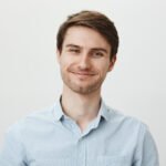 Keep talking but I do not care. Portrait of polite bothered attractive office worker in casual shirt pulling fake smile and trying to look friendly while standing over gray background, being annoyed. Emotions concept